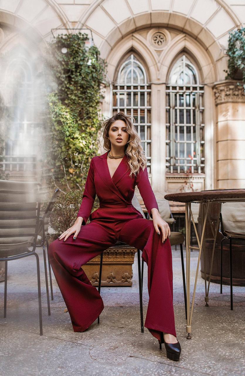 Woman in a red jumpsuit sitting in an elegant outdoor setting with architectural elements.