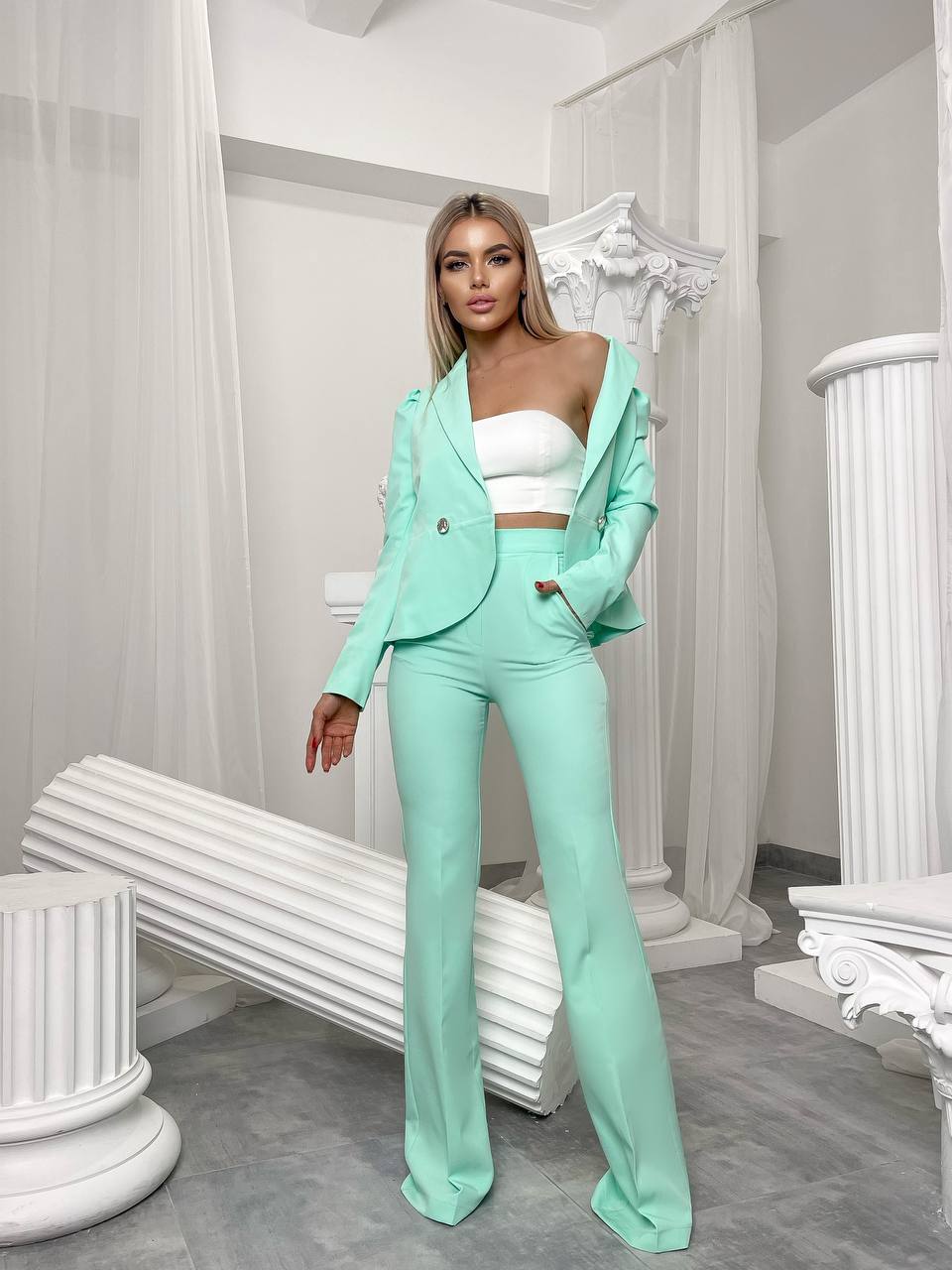 Woman in a mint green suit standing in an elegant room with white columns.