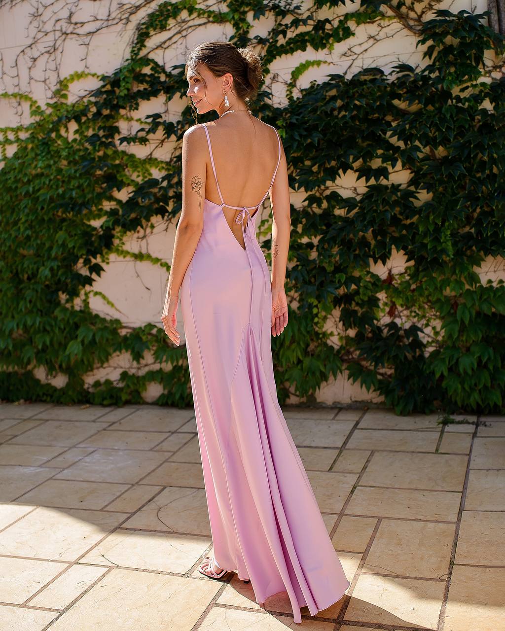 Woman in a pink evening gown standing against a wall with greenery