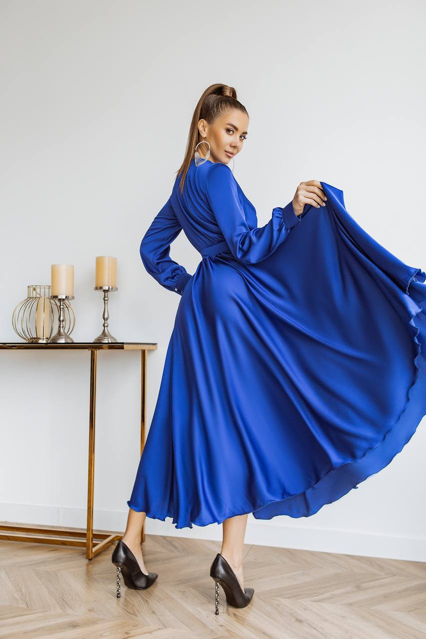 Woman in a blue dress posing in a room with candles on a table.