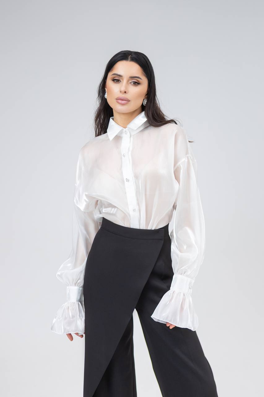 Woman wearing a white blouse and black pants against a gray background