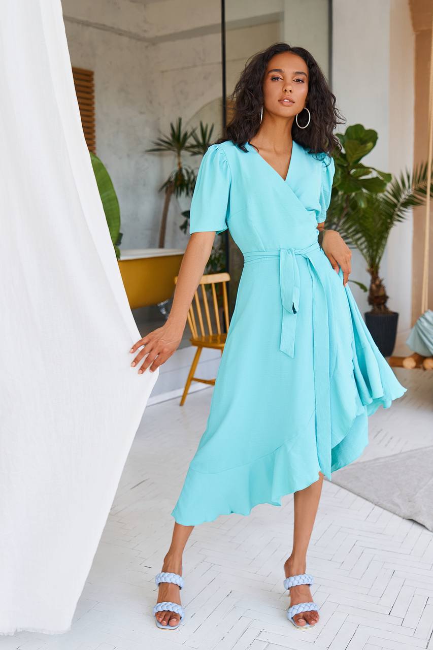Woman wearing a light blue dress in an indoor setting with plants and furniture.