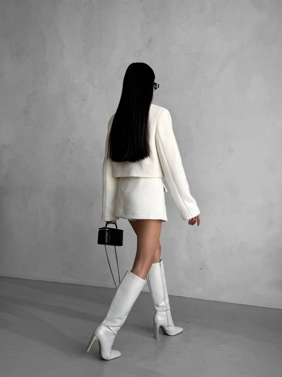 Person wearing a white outfit with knee-high boots against a gray background