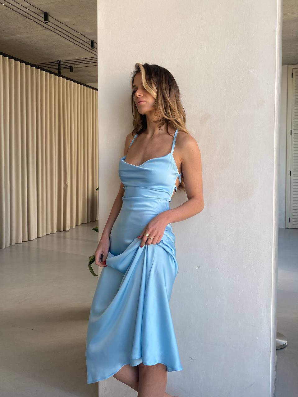 Woman in a light blue dress standing against a white wall.