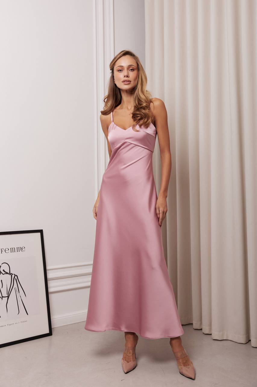 Woman wearing a pink satin dress standing against a white curtain.
