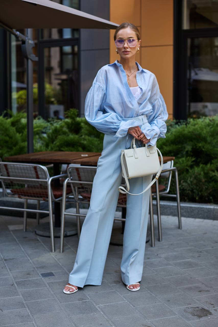 Woman in light blue outfit standing outdoors with tables and chairs in the background