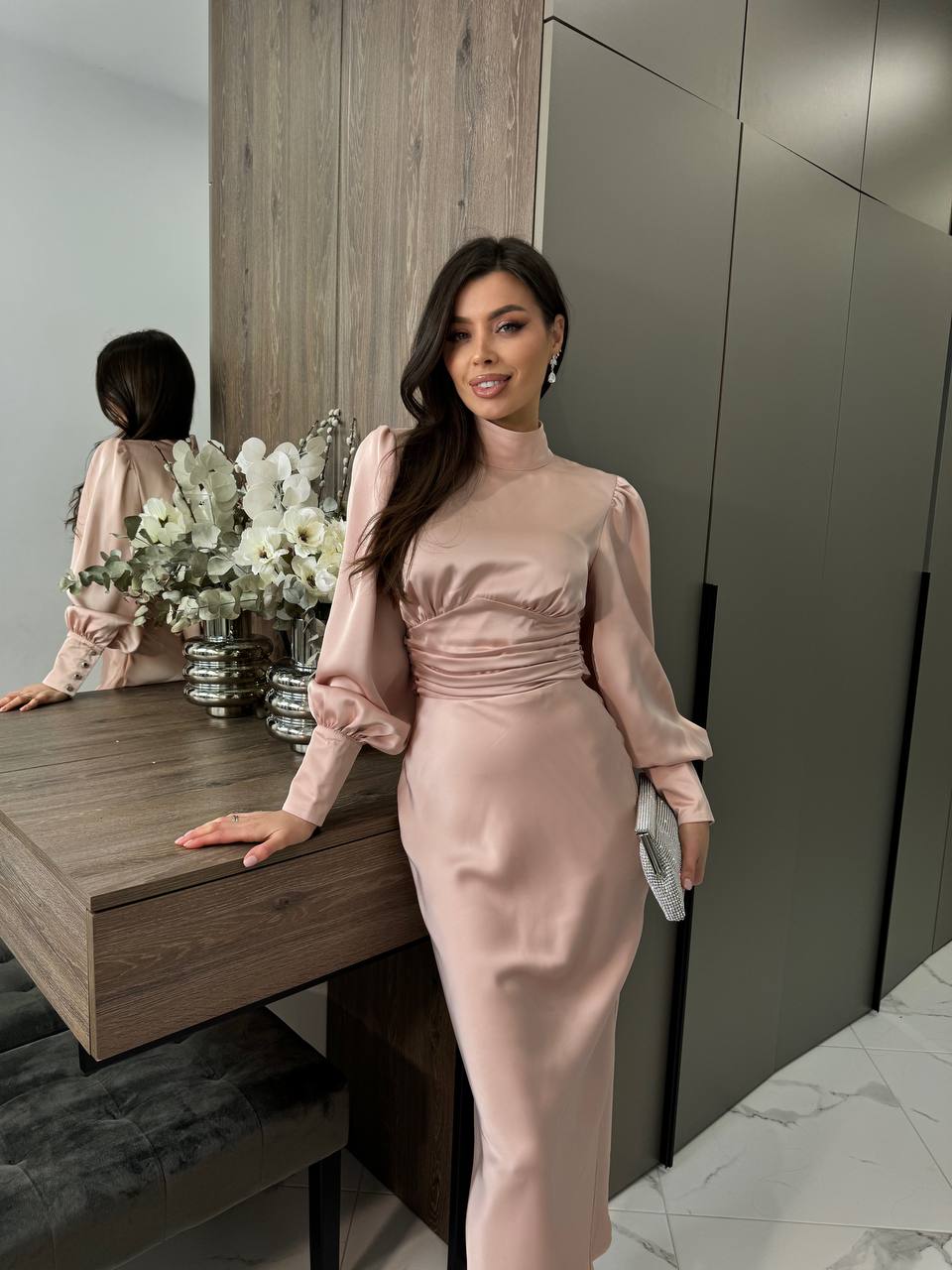 Woman in a pink satin dress standing in a modern interior setting.