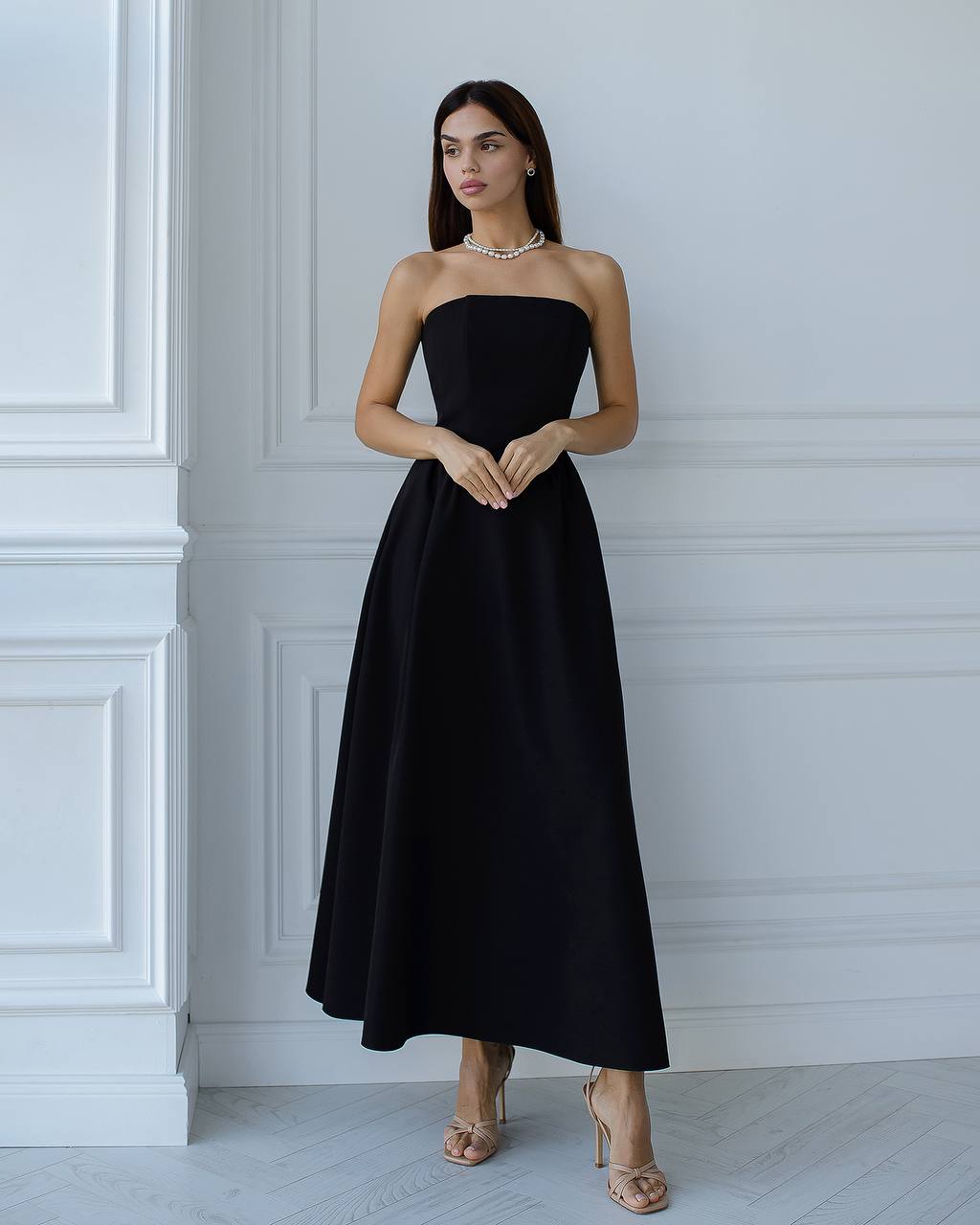 Woman wearing a black strapless dress against a white wall