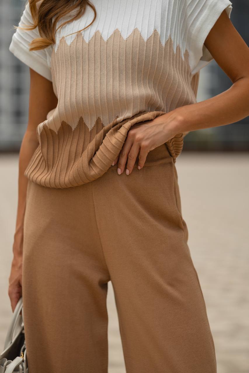 Person wearing a beige top and brown pants with a blurred background