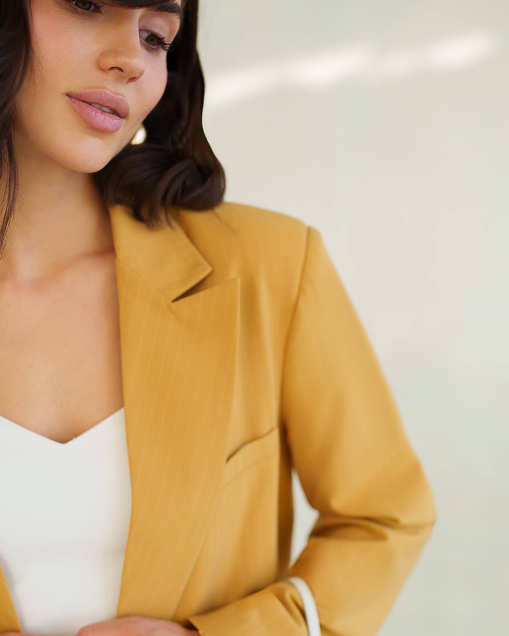 Woman wearing a mustard yellow blazer over a white top against a light background
