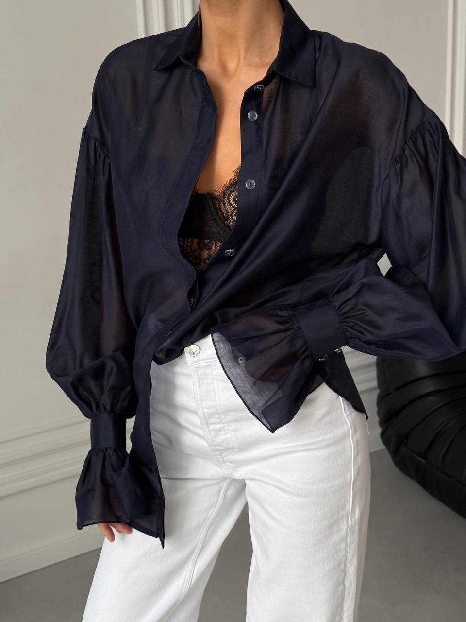 Person wearing a black oversized shirt over a black top and white pants in a neutral setting