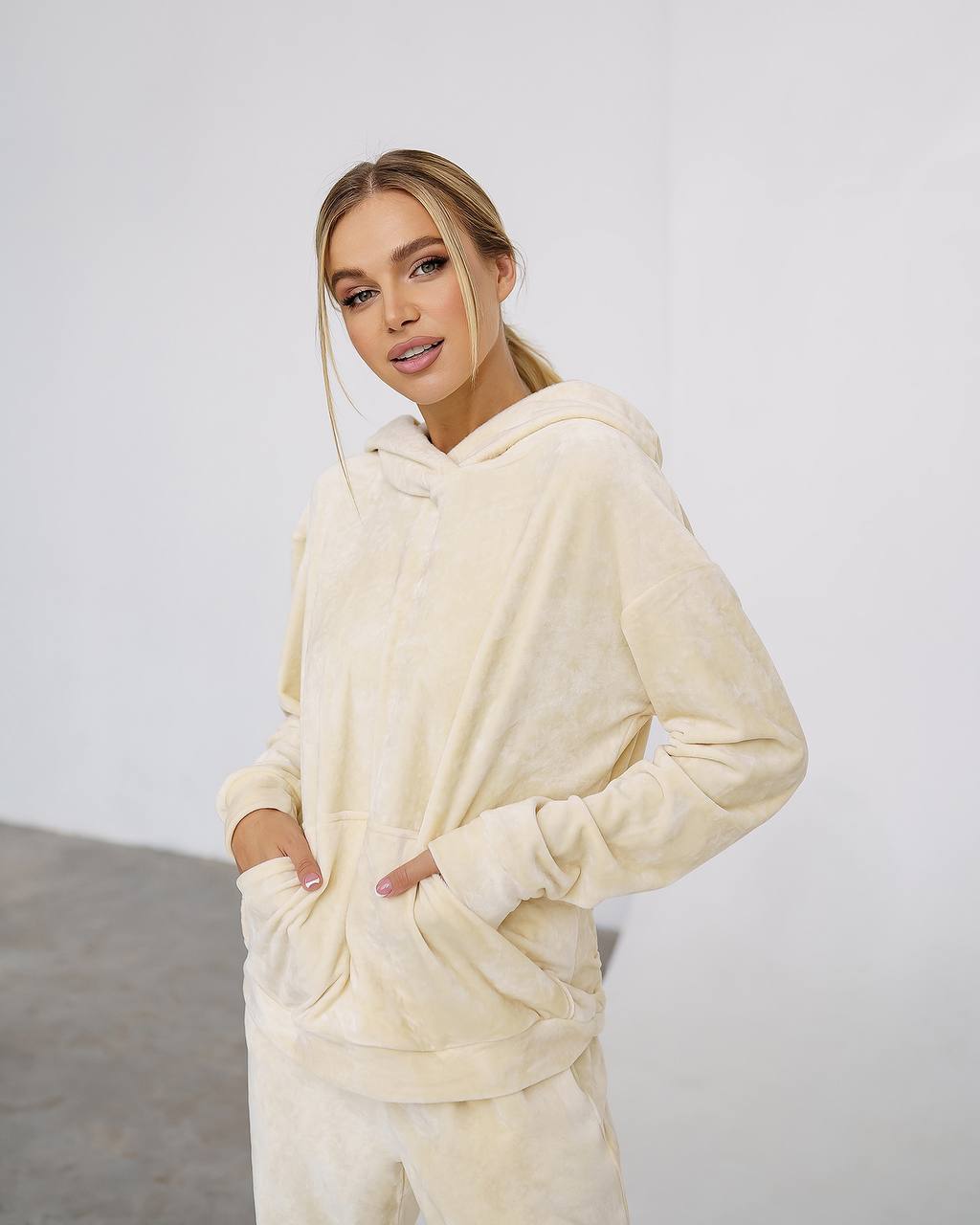 Woman wearing a cream-colored hoodie and pants against a plain background