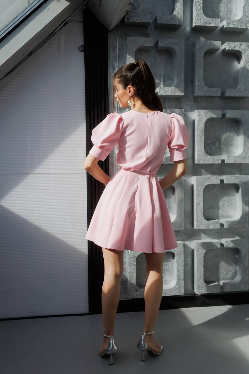 Woman in a pink dress standing against a textured wall.
