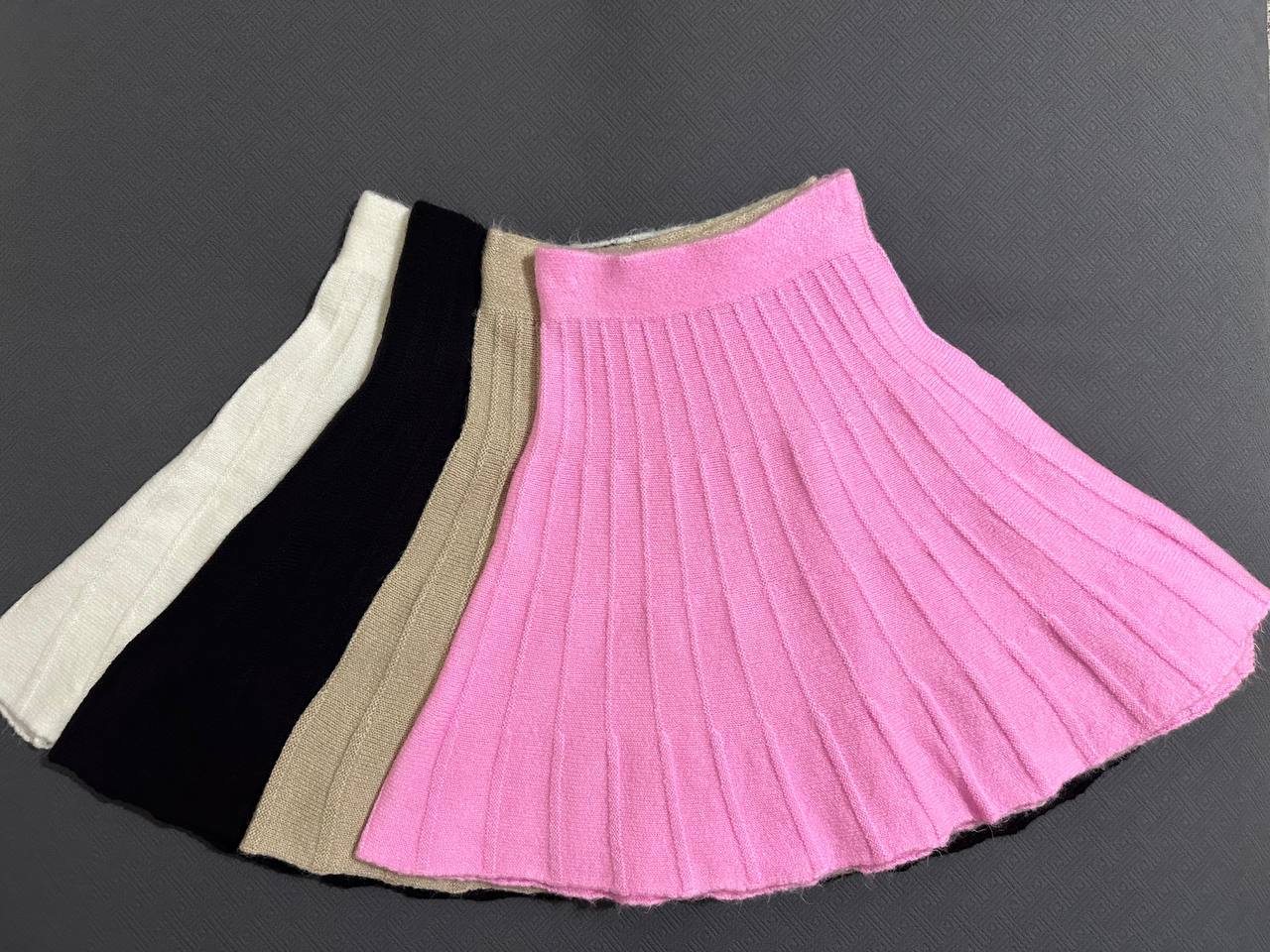 Three pleated skirts in white, black, and pink on a dark background