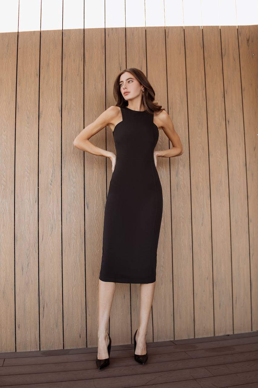 Woman in a black dress standing against a wooden wall