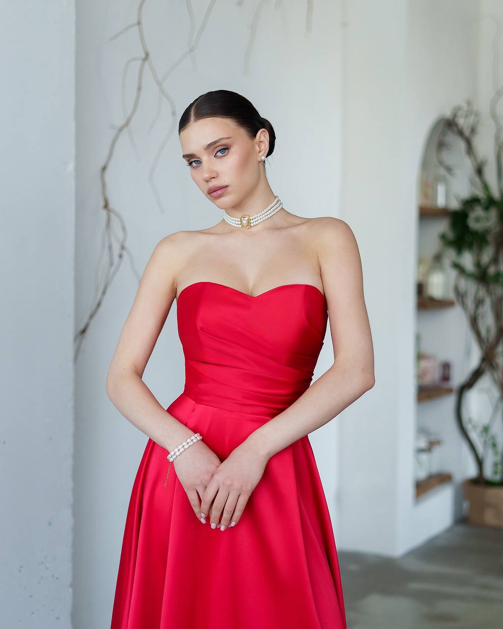 Woman wearing a red strapless dress with jewelry indoors.