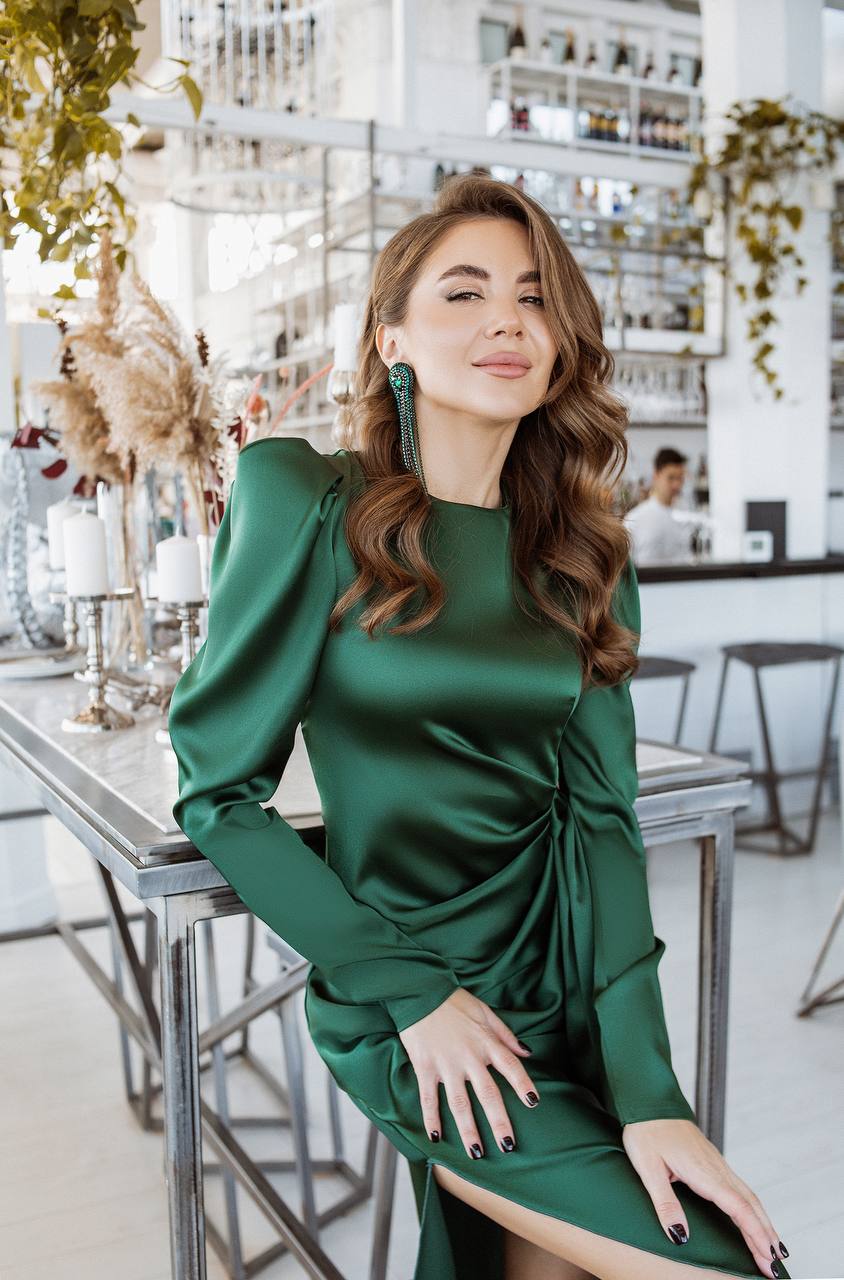 Woman in a green dress sitting at a table in an indoor setting.