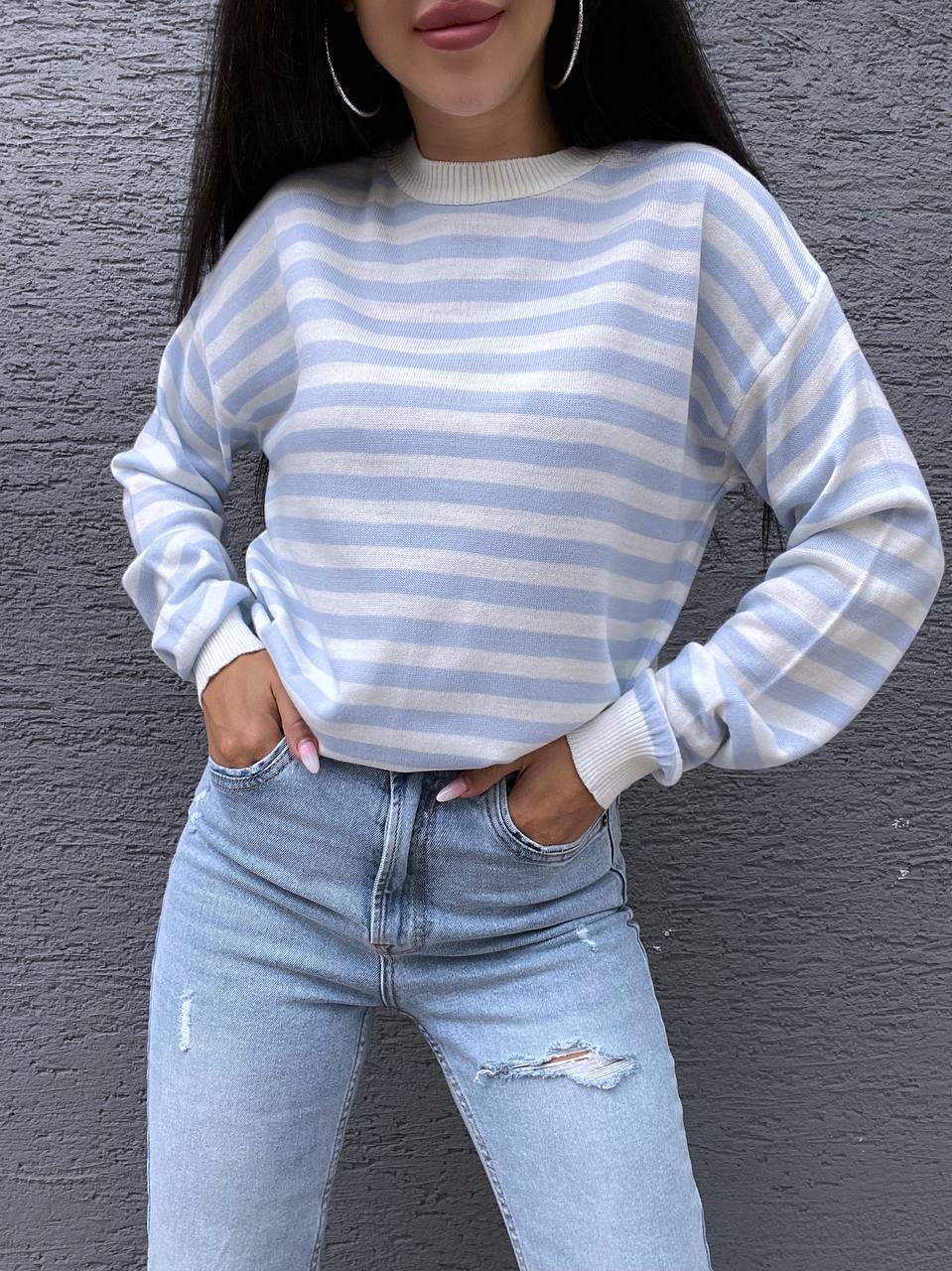 Person wearing a blue and white striped sweater and light blue jeans against a gray background