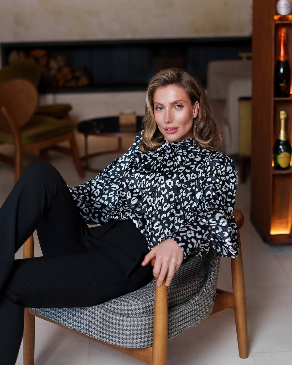 Woman sitting on a chair in a room with a fireplace and shelves.