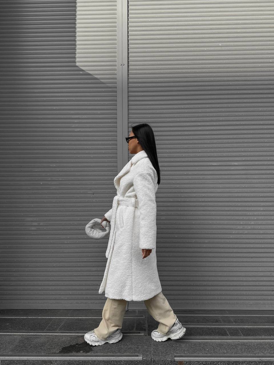 Person wearing a white coat walking past a metallic wall.