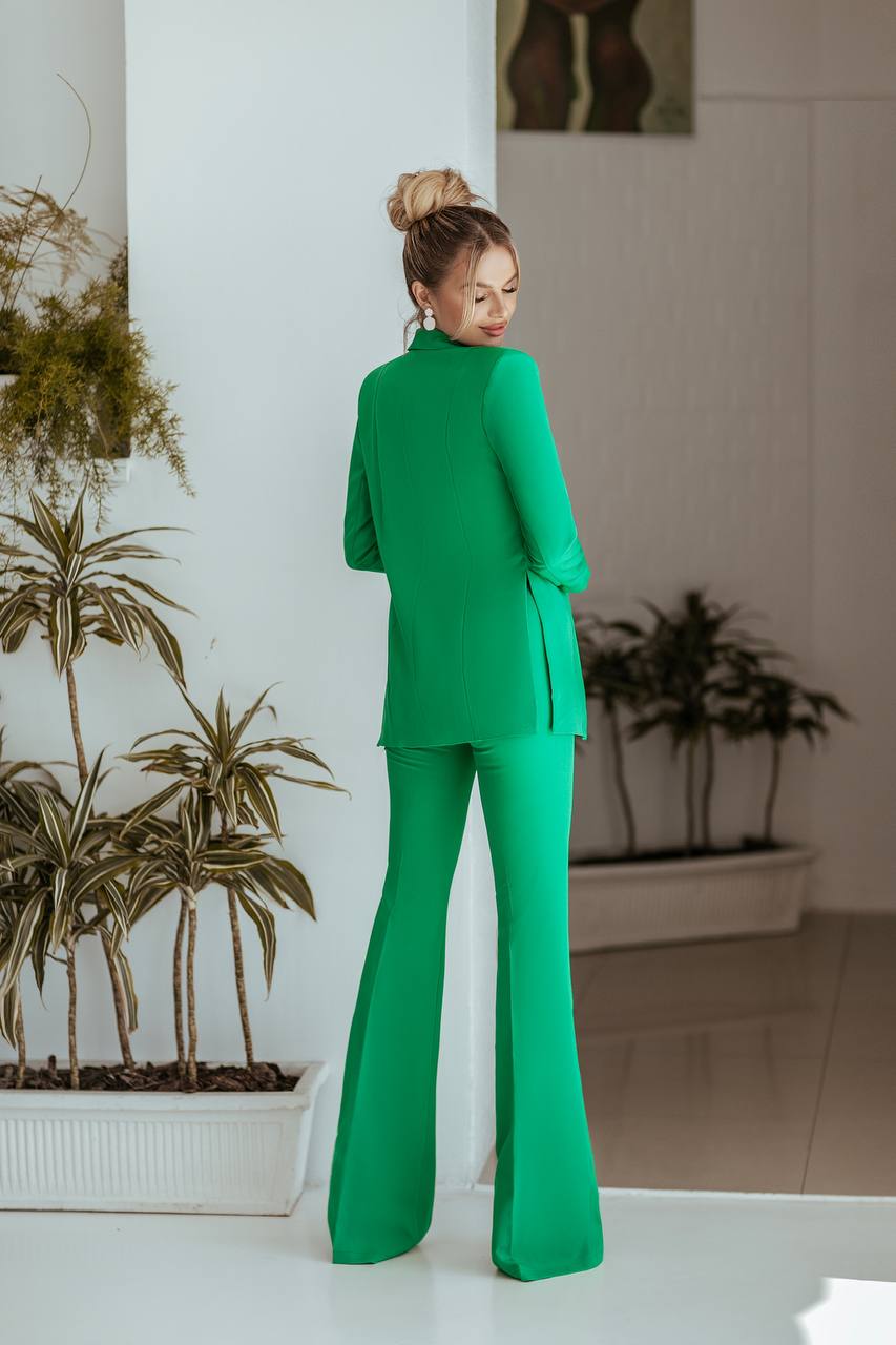 Woman in a green suit standing in a room with plants.