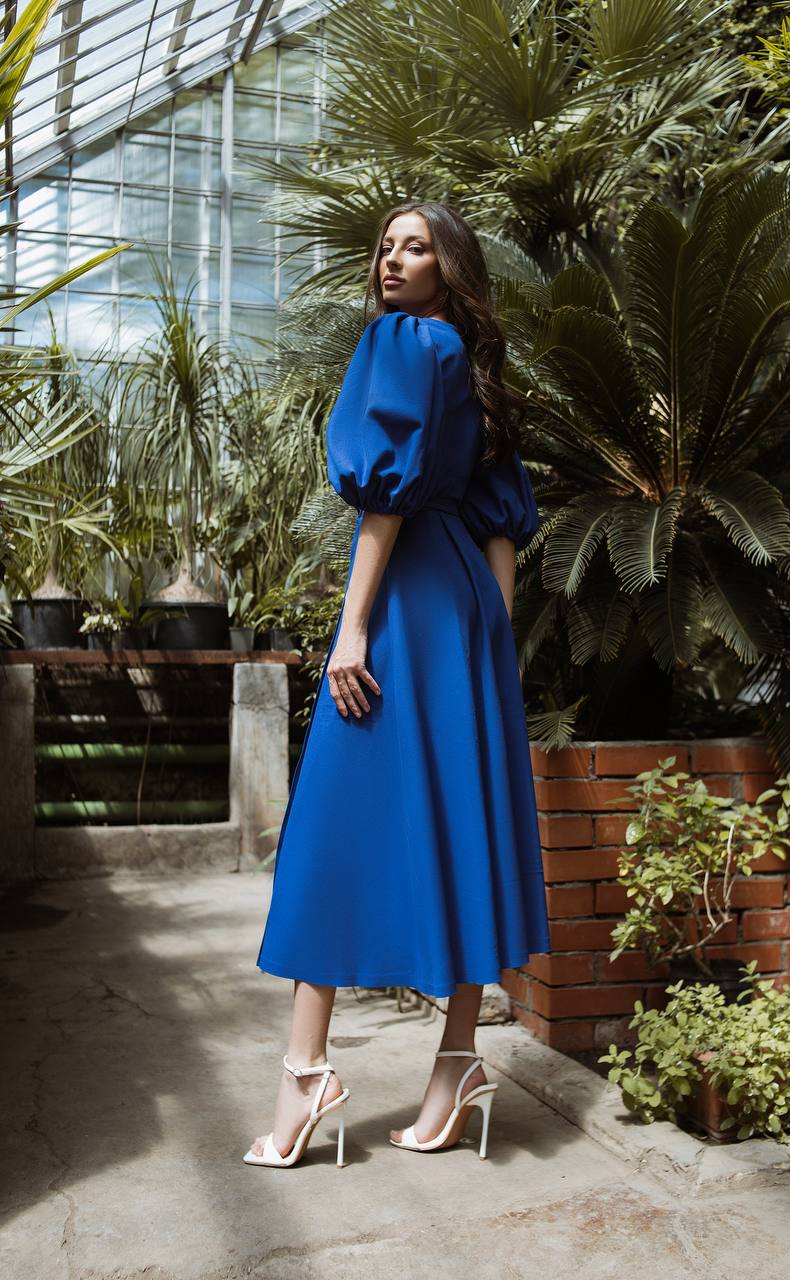 Woman in a blue dress standing in a greenhouse with plants around