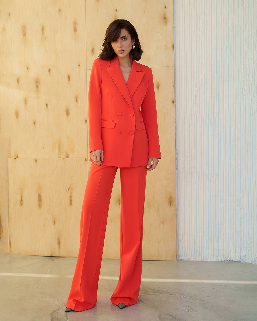 Woman wearing a bright red suit standing against a wooden wall.