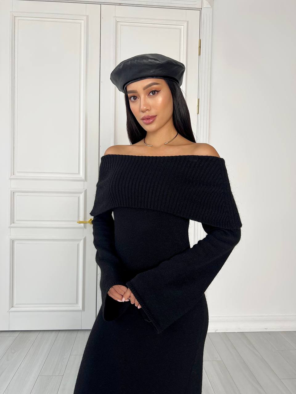 Woman wearing a black off-shoulder dress and cap indoors.