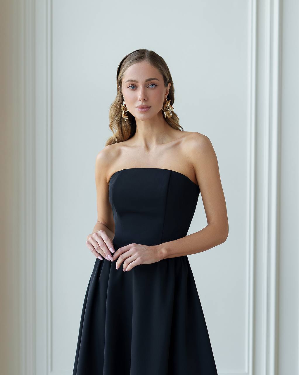 Woman wearing a strapless black dress against a light gray wall