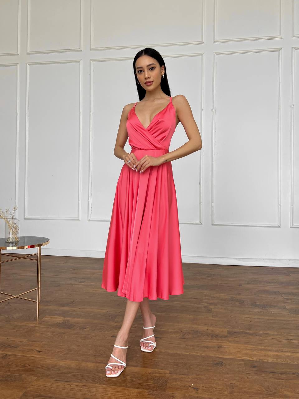 Woman in a pink dress standing in a room with wooden flooring and white paneled walls.