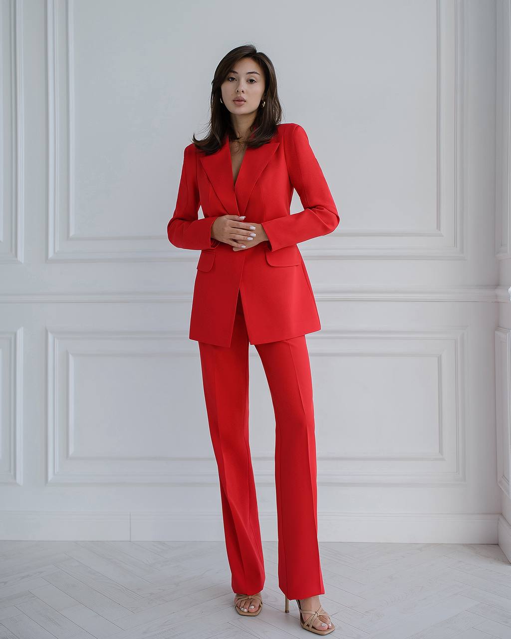 Woman wearing a red suit standing against a white paneled wall.