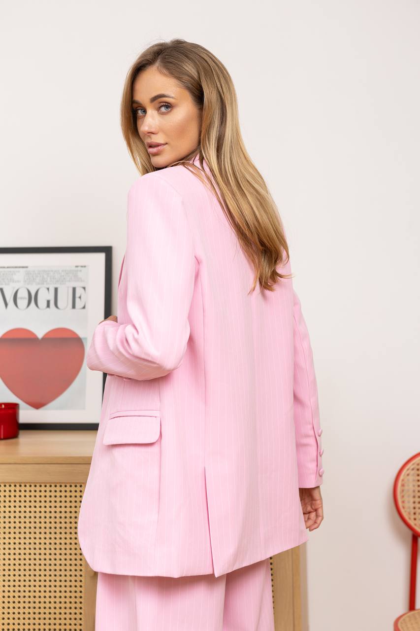 Woman wearing a pink suit standing in a room with a 'Vogue' magazine in the background.