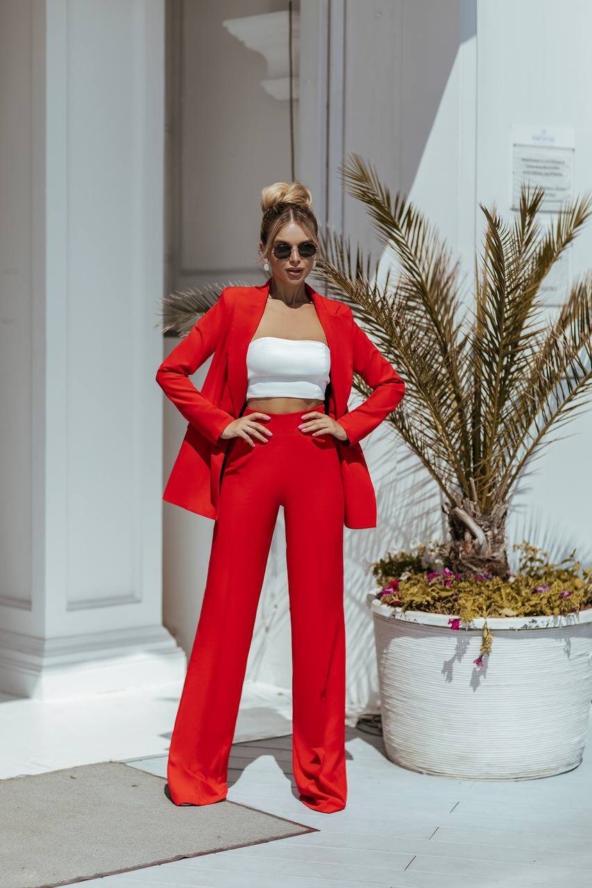 Woman in a red outfit standing outdoors with plants and columns in the background