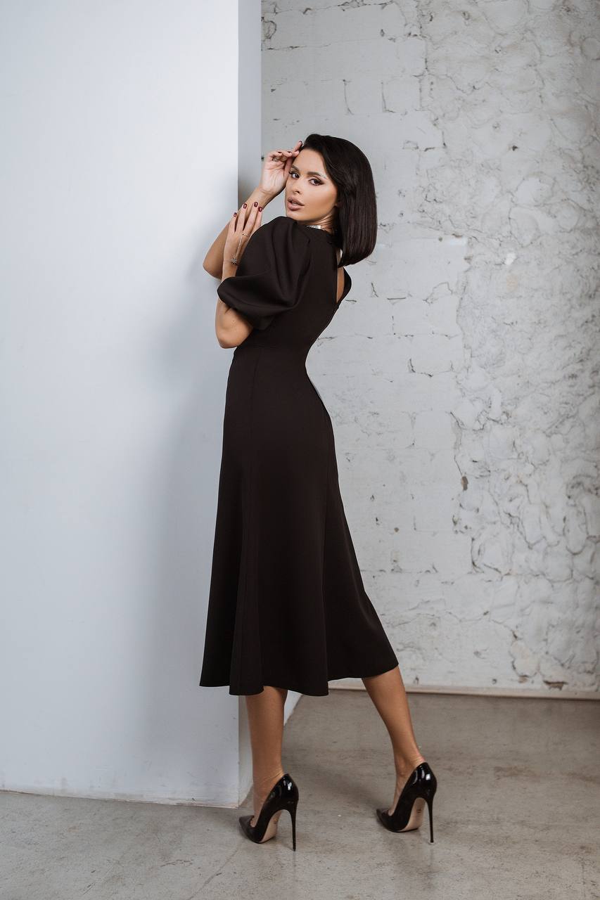 Woman in a black dress standing against a textured wall.