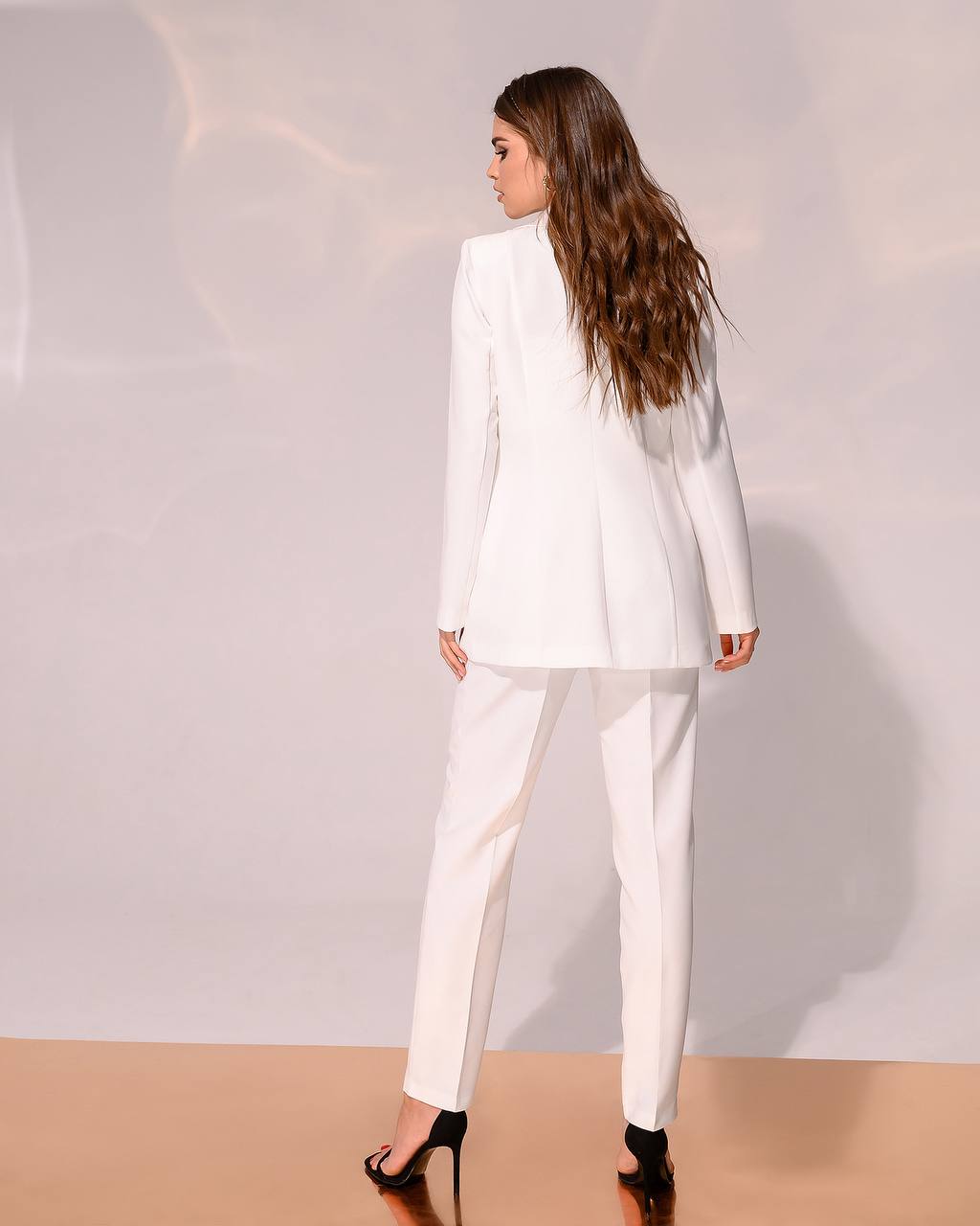 Woman wearing a white suit standing against a plain background