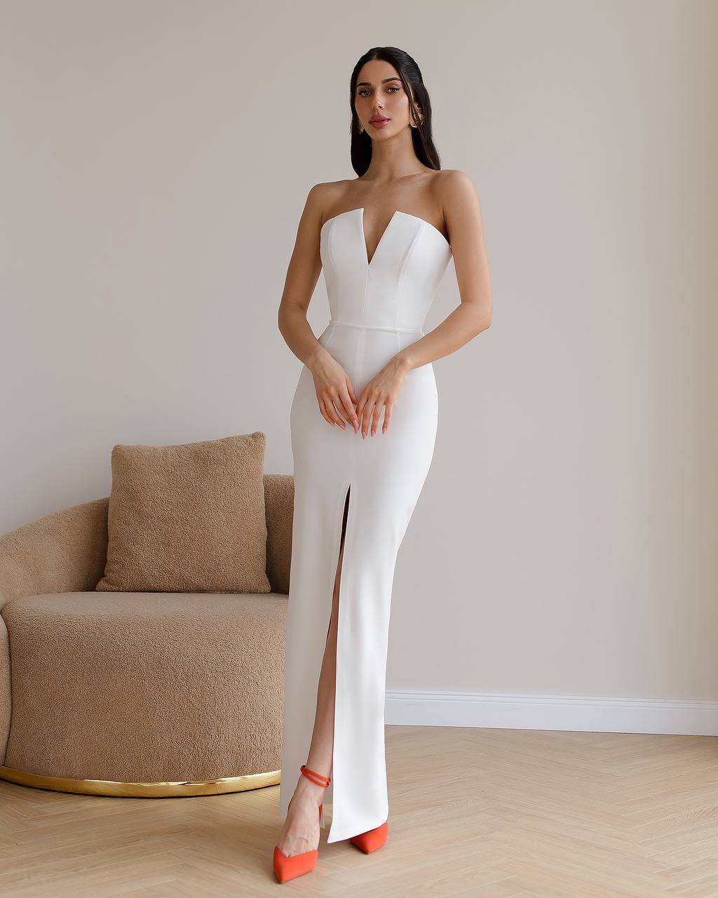 Woman in a white strapless gown with a high slit standing in a minimalistic room.