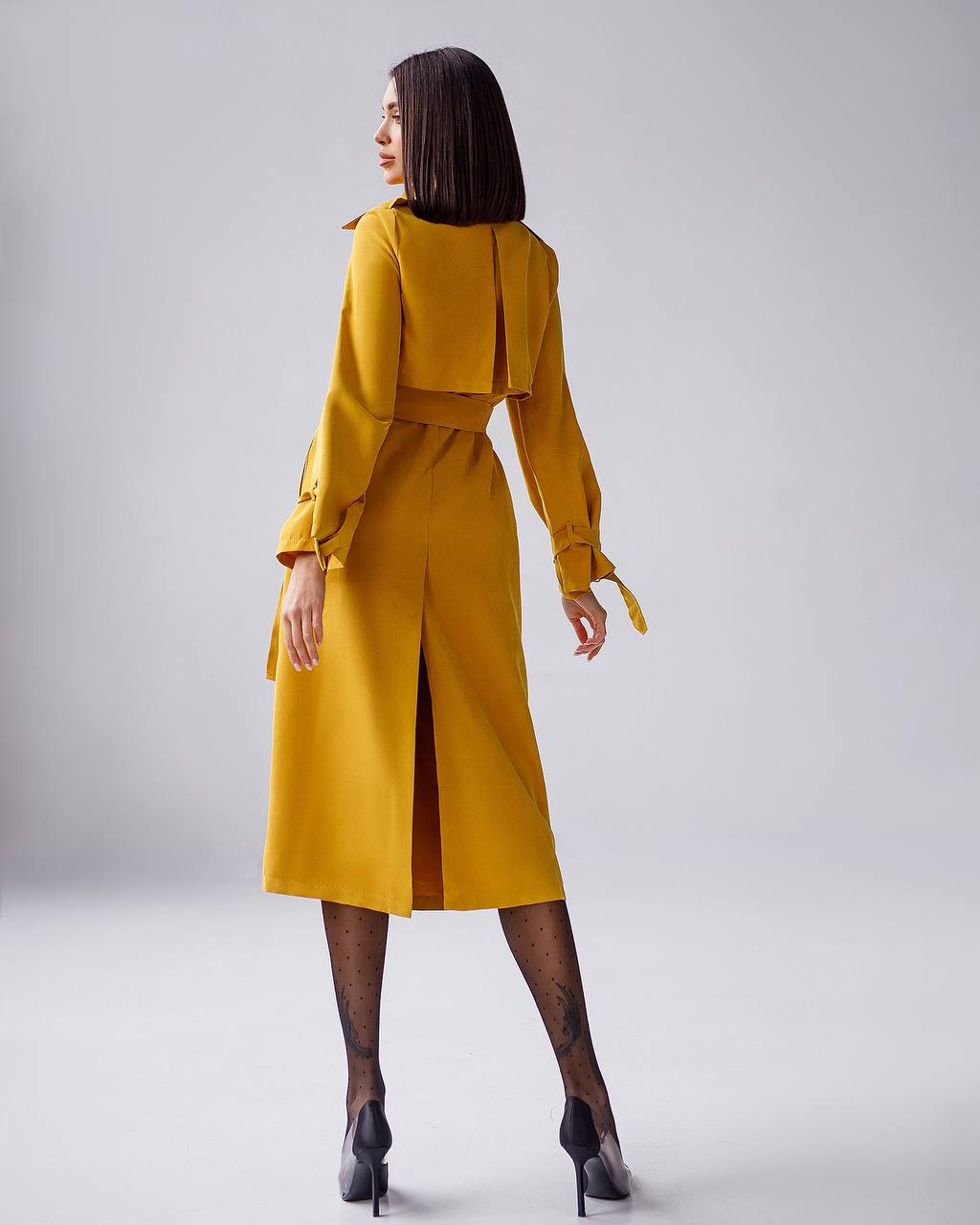 Woman wearing a mustard yellow dress with a belt on a light gray background