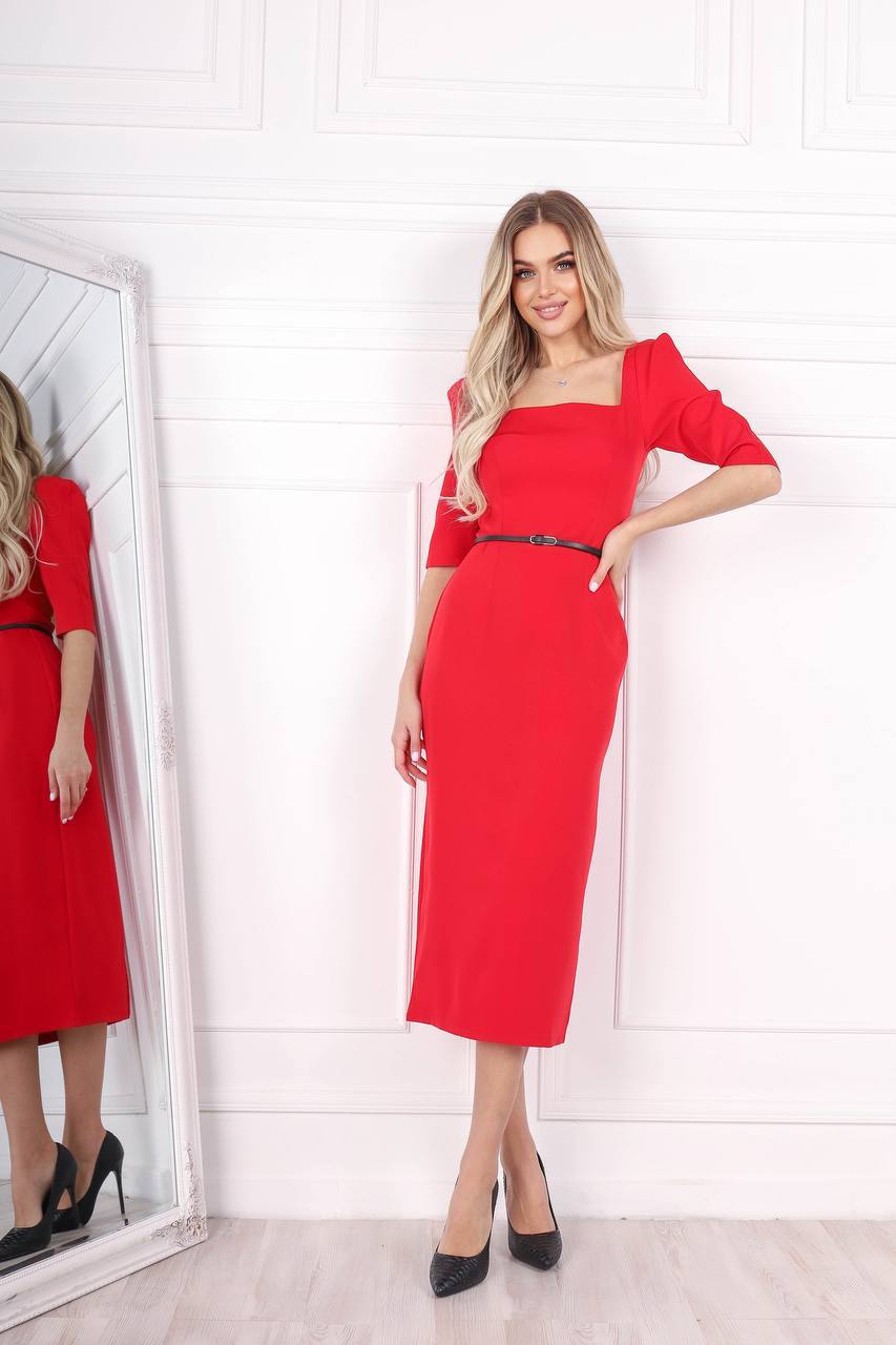 Woman wearing a red dress standing next to a mirror in a room with white walls.