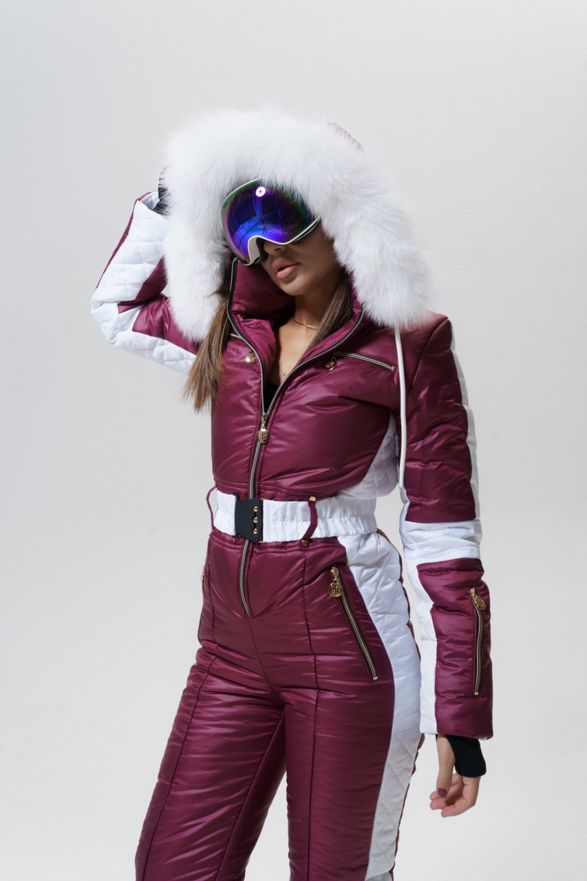 Person wearing a maroon and white ski suit with goggles on a plain background