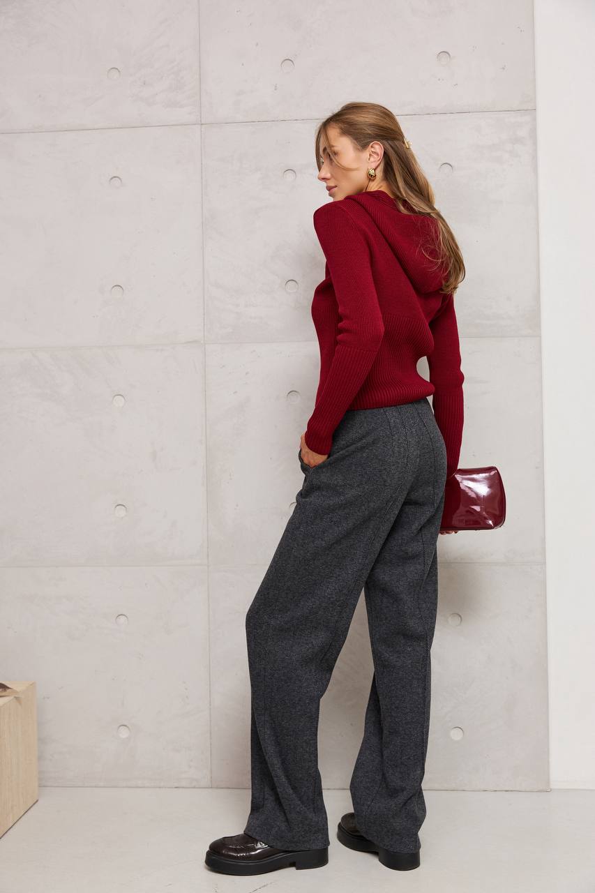 Person wearing a red hoodie and gray pants against a light gray wall.