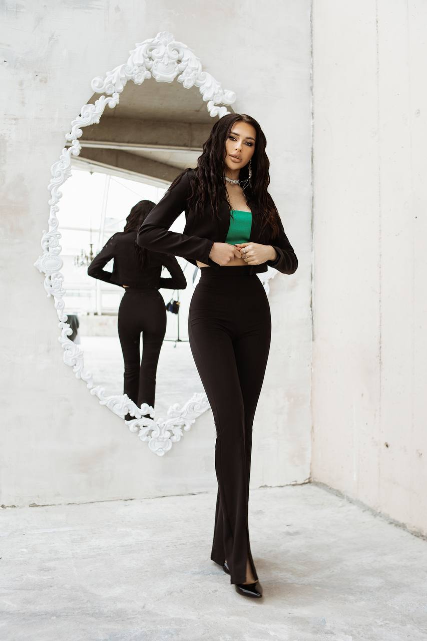 Woman in a black outfit standing in front of a decorative mirror.