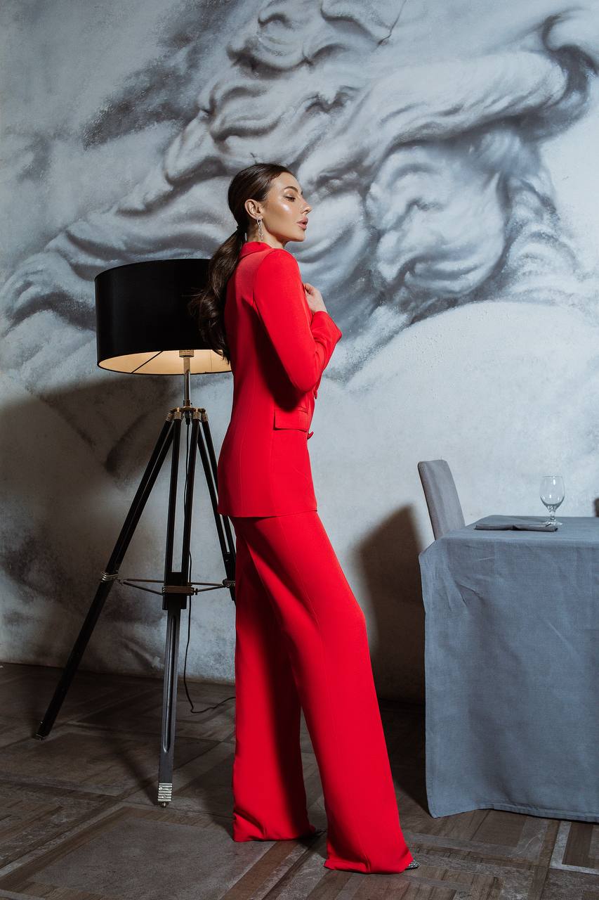 Woman in a red outfit standing in a room with a decorative wall and lamp.