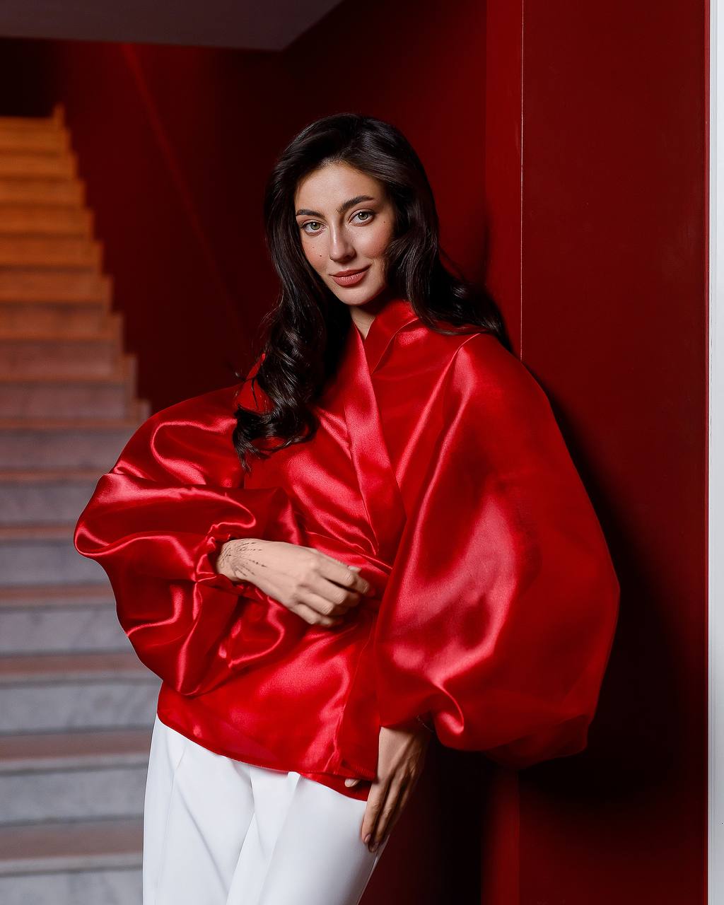 Woman wearing a red satin outfit against a red wall.