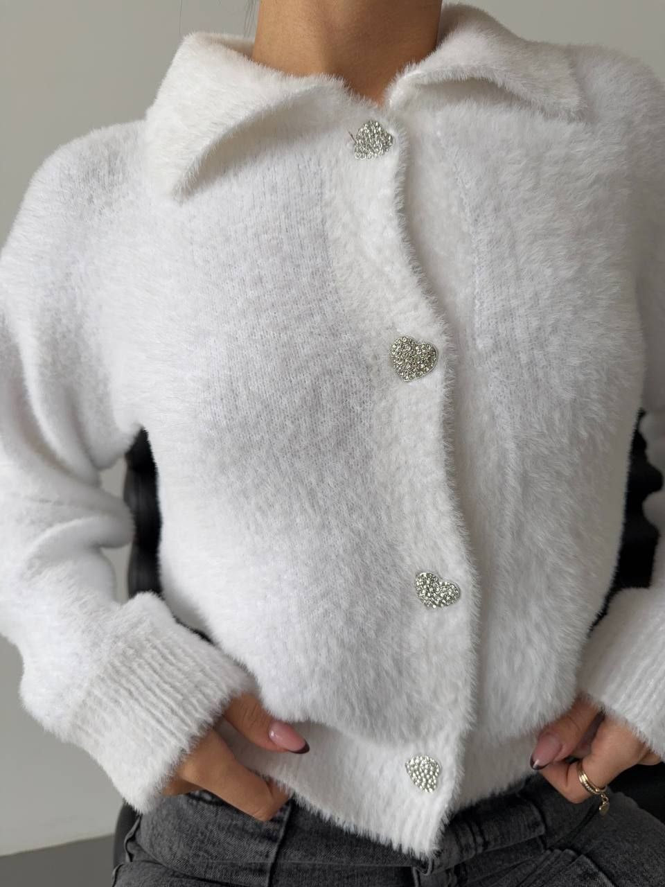 White fluffy cardigan with decorative buttons worn by a person against a neutral background