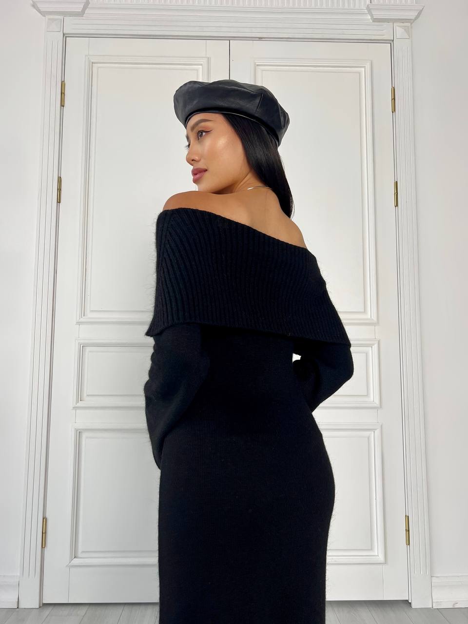 Woman wearing a black off-shoulder sweater and beret in front of a white door.