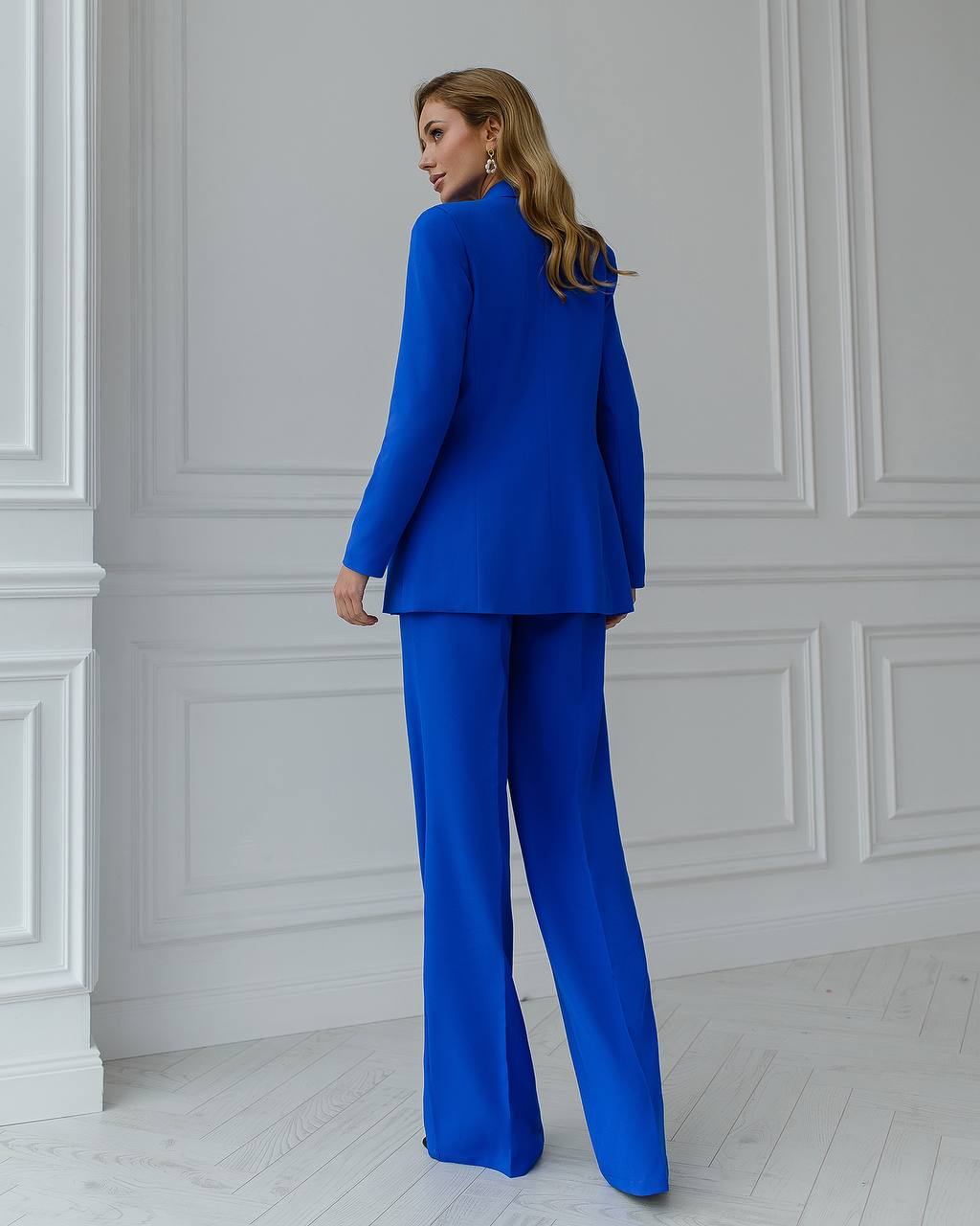 Woman wearing a blue suit standing against a white paneled wall.