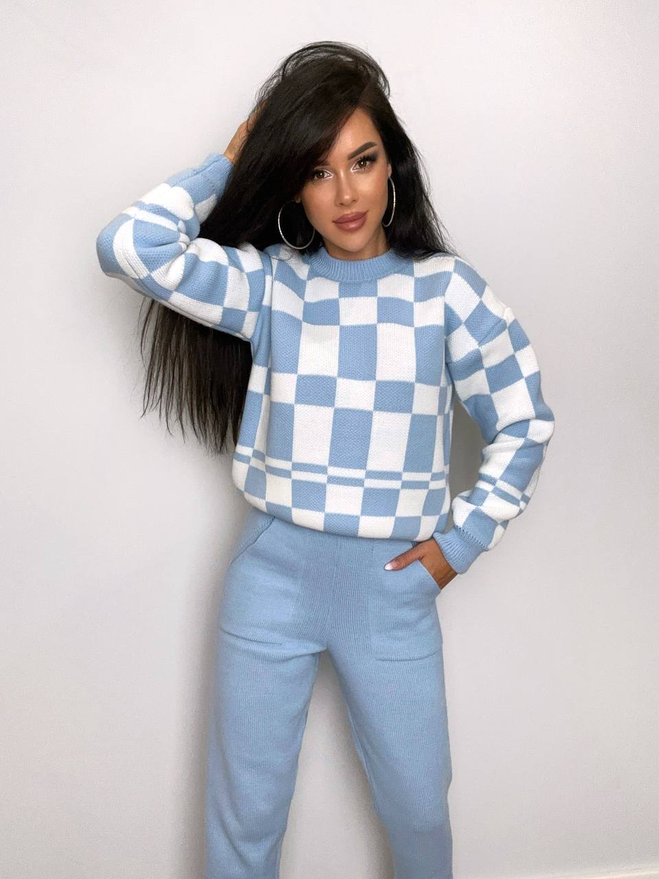 Woman wearing a blue and white checkered sweater and pants against a plain background