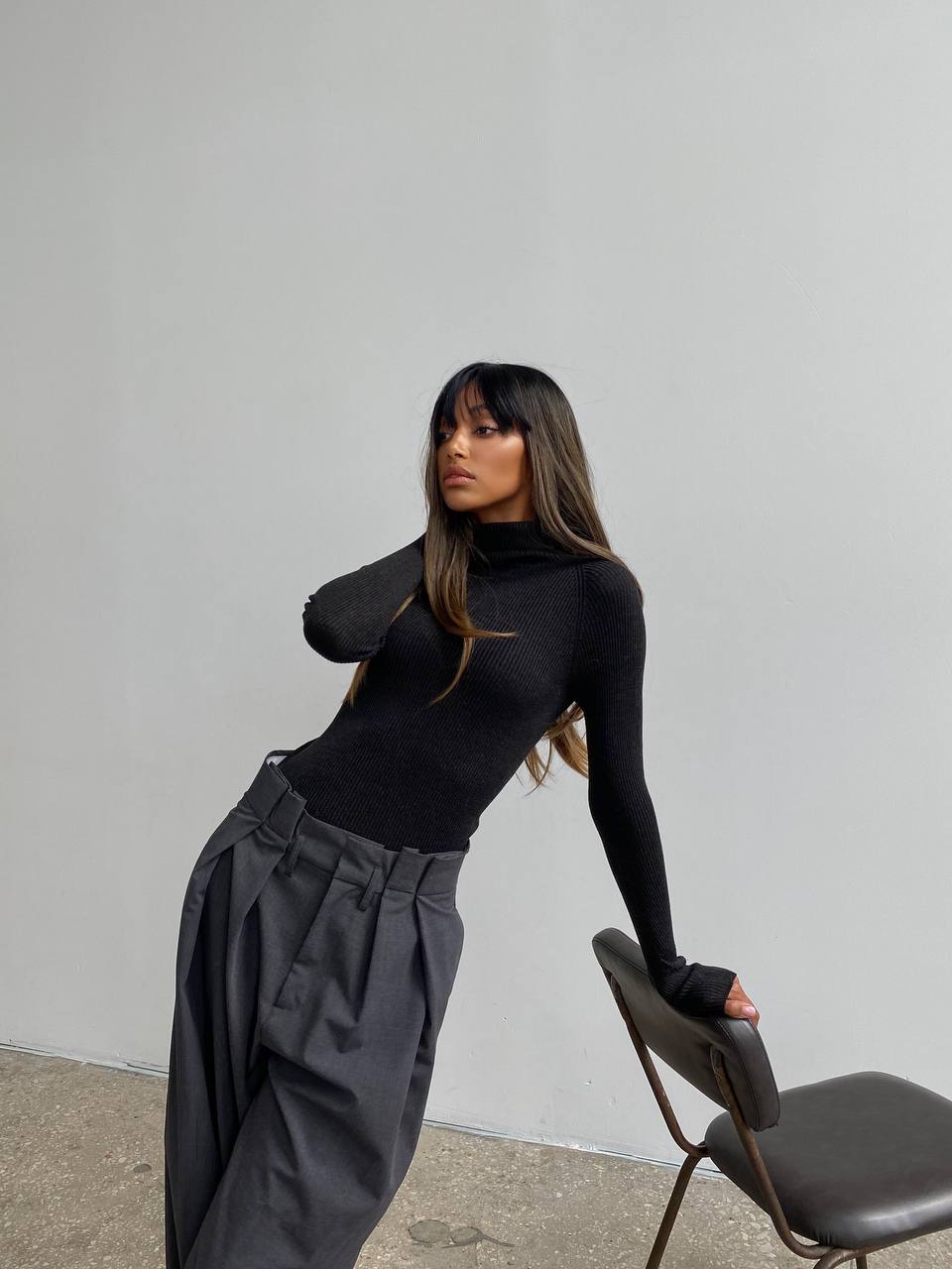 Person wearing a black turtleneck and dark pants against a plain background