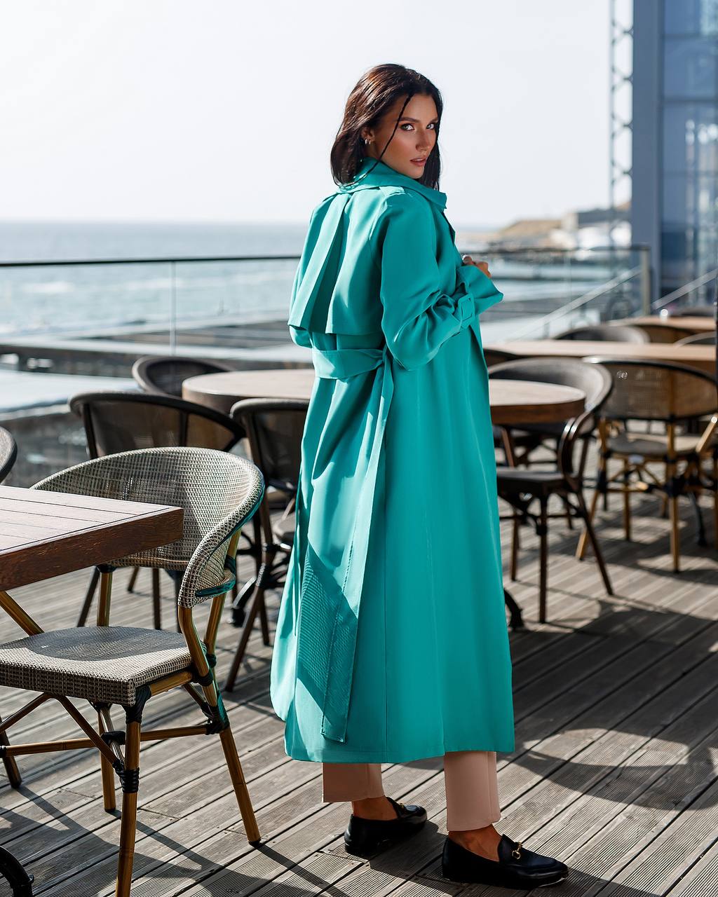 Woman in a teal coat standing on a rooftop with ocean view