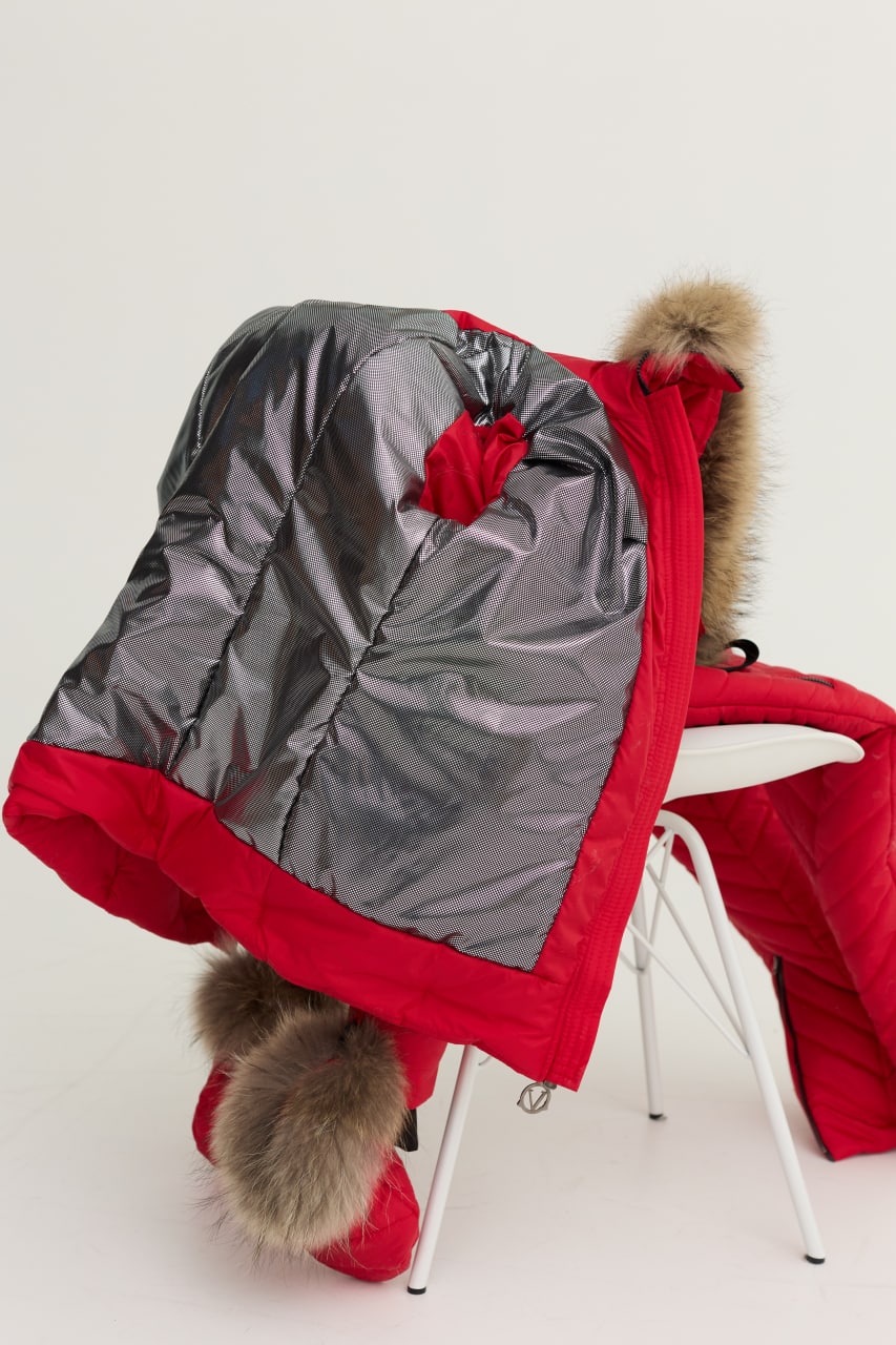 Red winter coat with gray hood and fur trim on a white chair against a white background